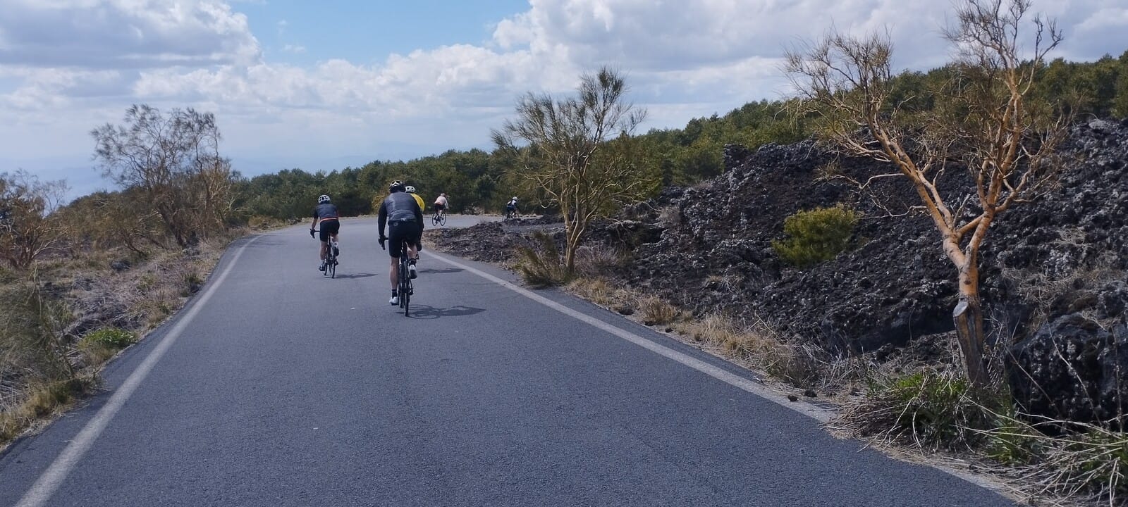 Cyclists riding past lava flows on the slopes of Mount Etna