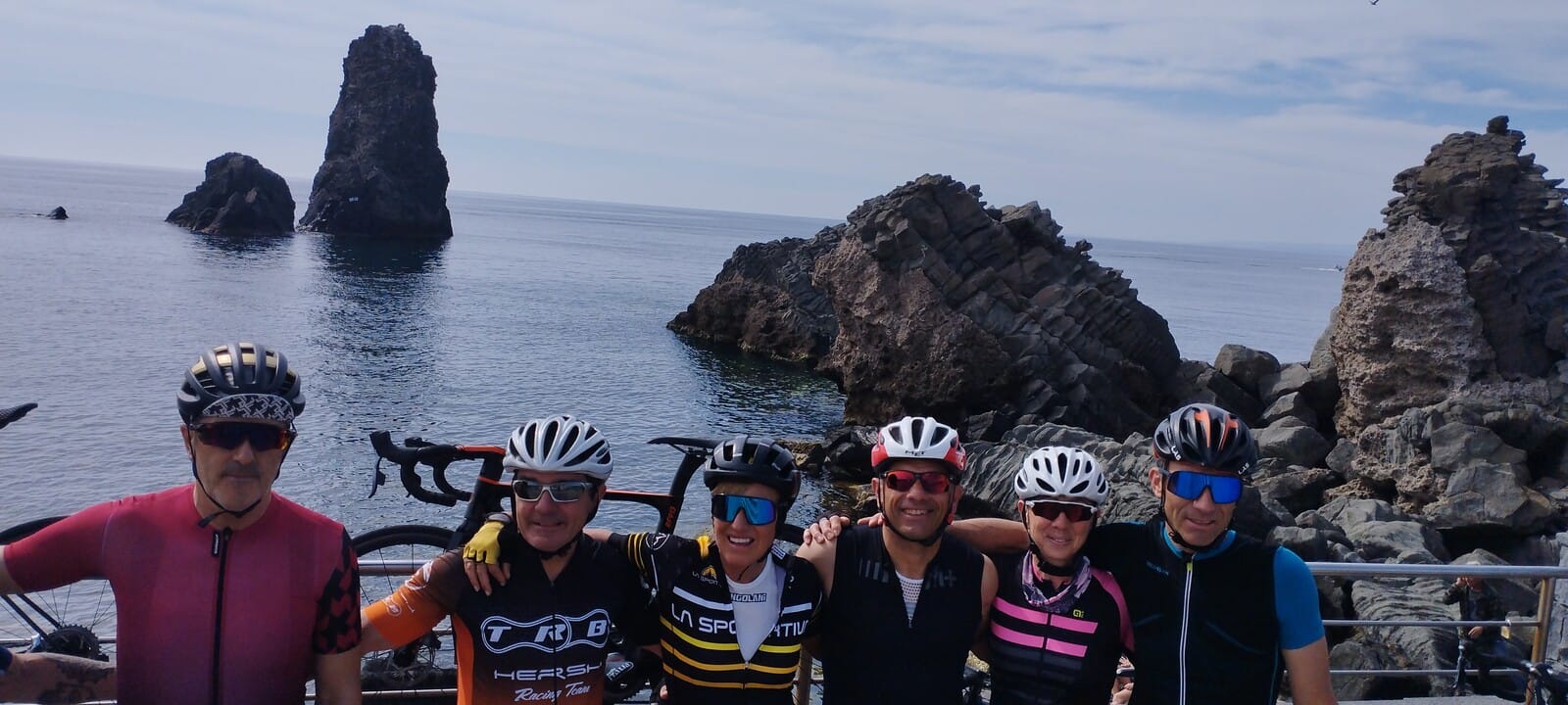 Group of cyclists posing along Sicily's rocky coastline