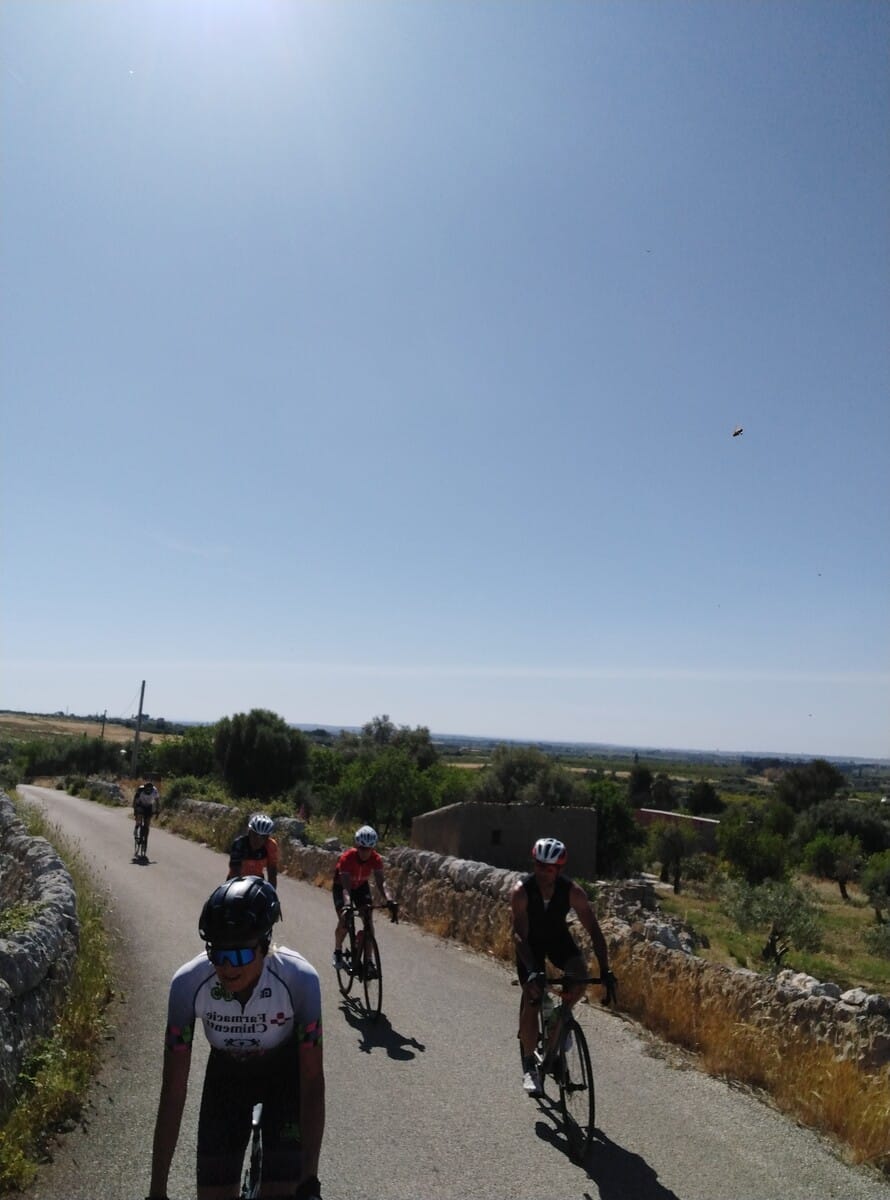 Cyclists riding along a stone-walled countryside road in Sicily